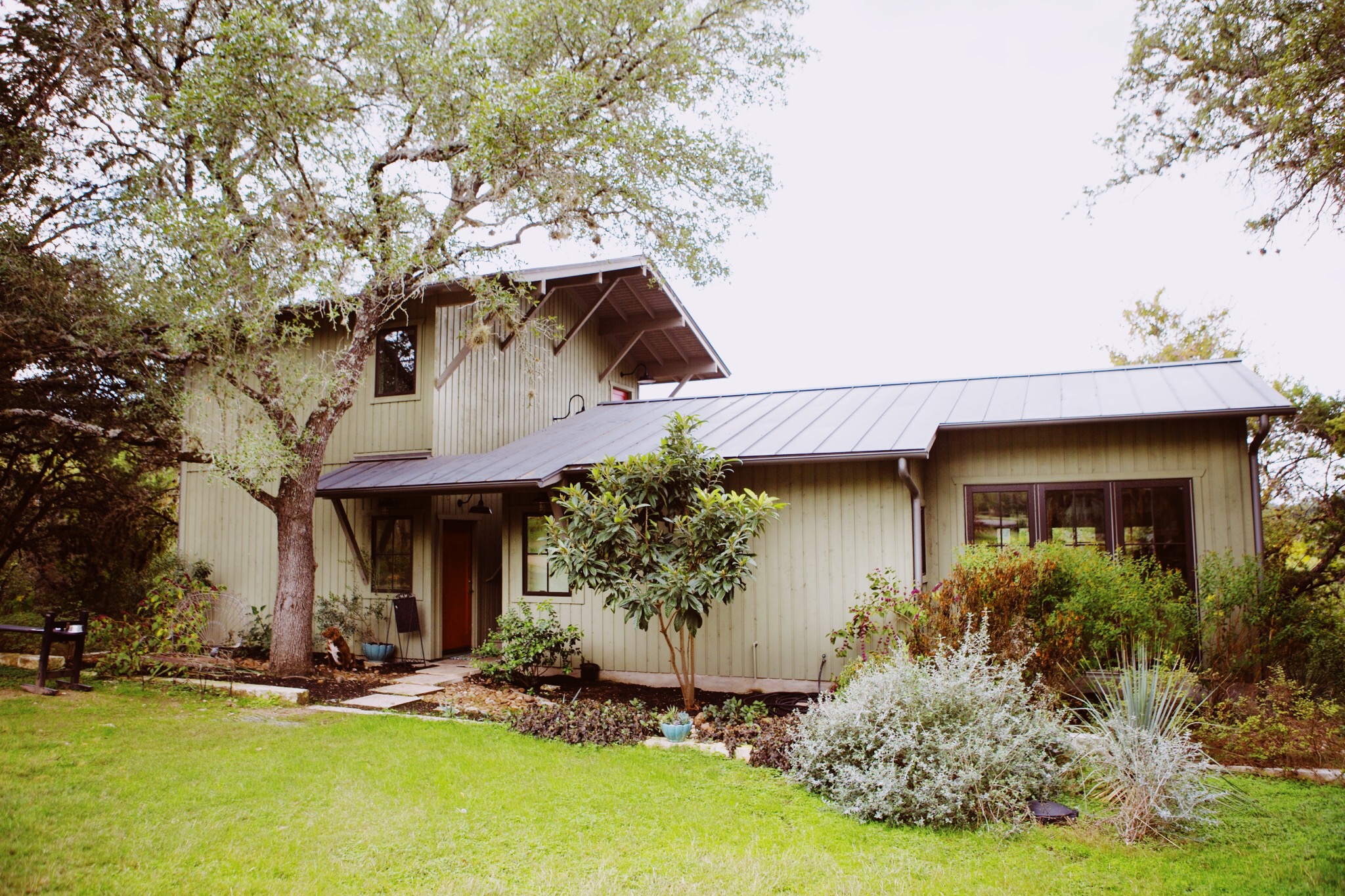 Baskin House A green house with one and two stories, a rain chain, and a metal roof.